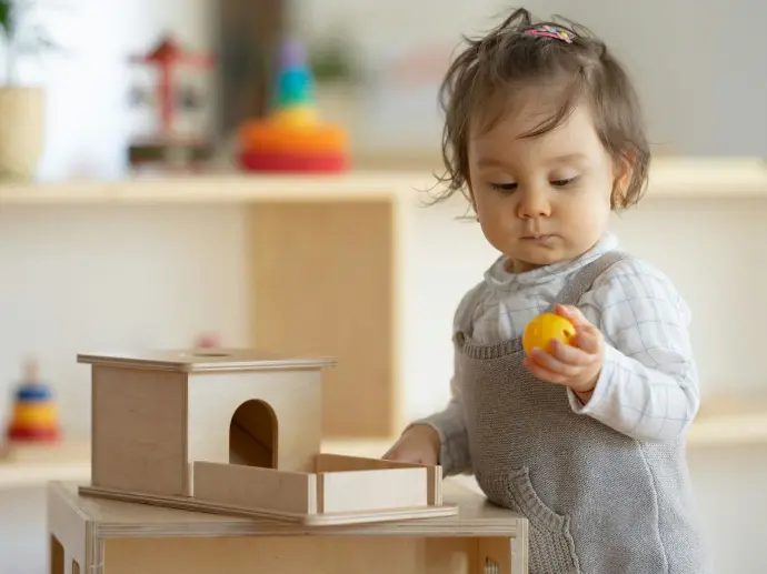 Enfant que le parent peut observer, en train de manipuler une balle à emboiter dans un jouet en bois type Montessori